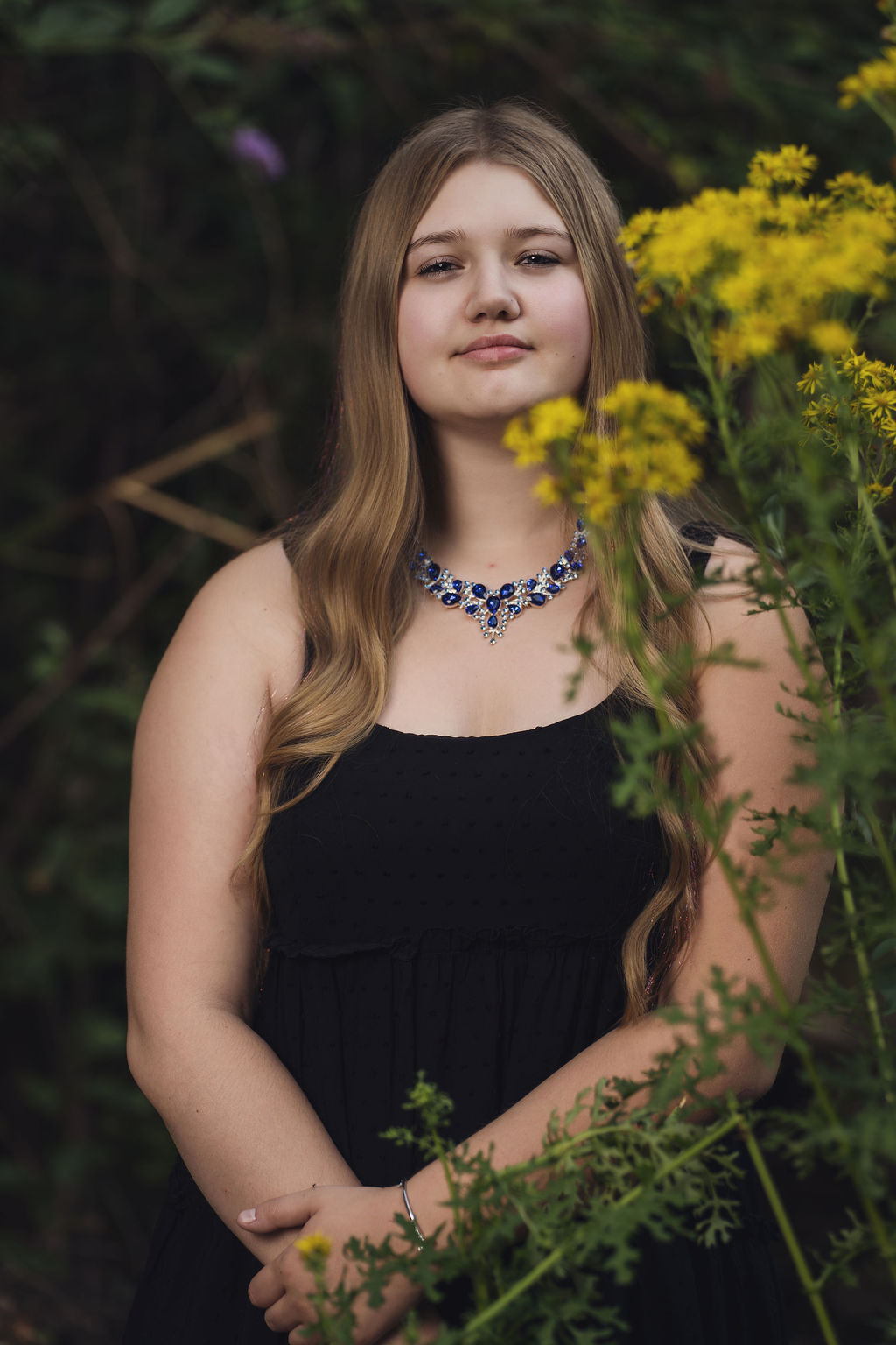 Senior girl holding a stem of yellow wildflowers in a black dress at Belfair State Park