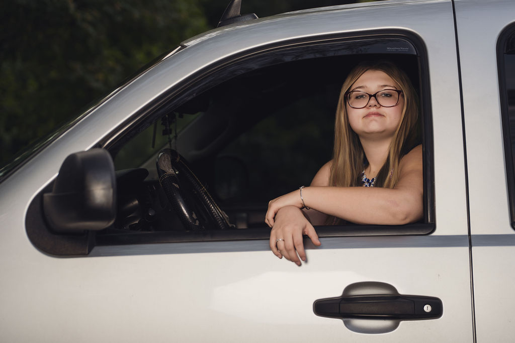 Senior leaning out the driver window of a silver Chevy pickup during her Belfair senior session