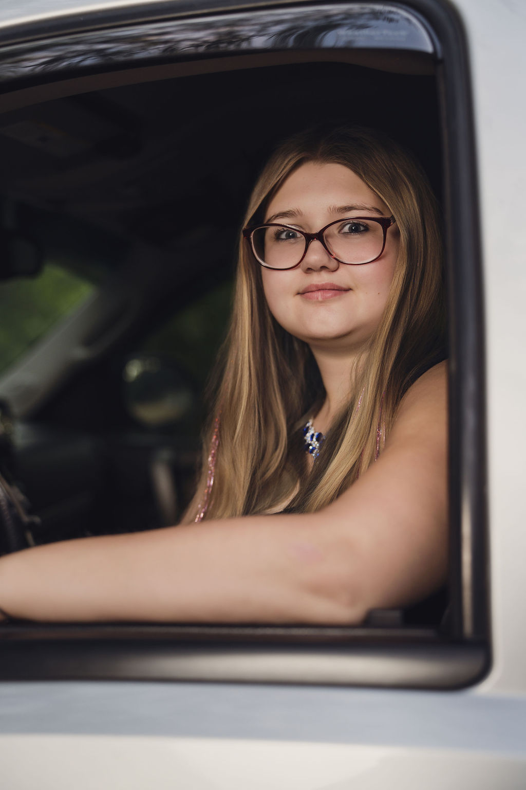Senior in a black dress resting her arm on the door of a silver Chevy pickup at Belfair State Park