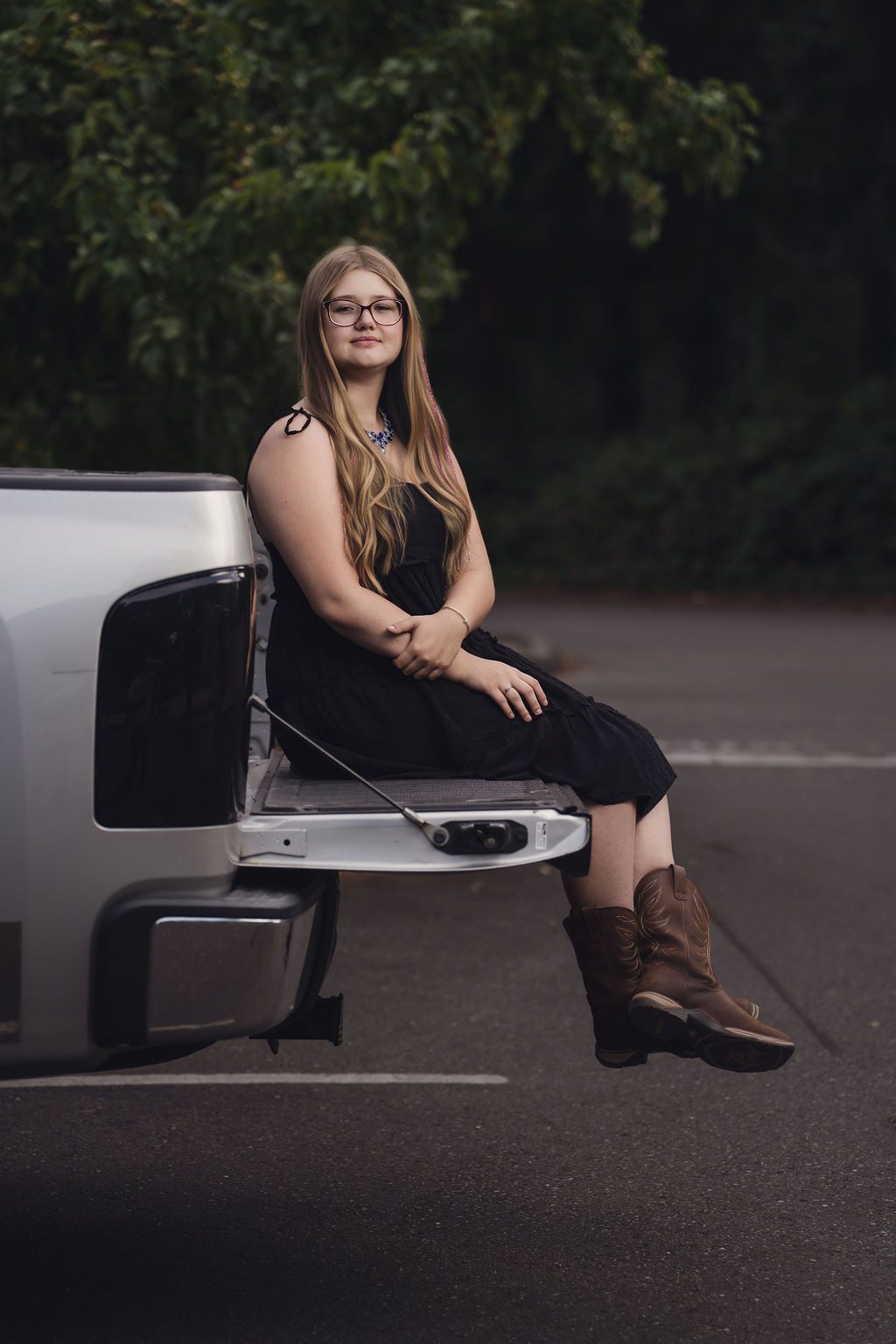 Senior in a black dress and cowboy boots seated on the tailgate of her pickup on the Kitsap Peninsula