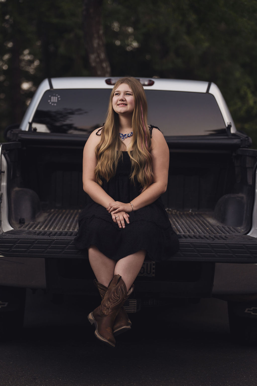 Senior girl seated on the open tailgate of a silver pickup with crossed cowboy boots near Hood Canal