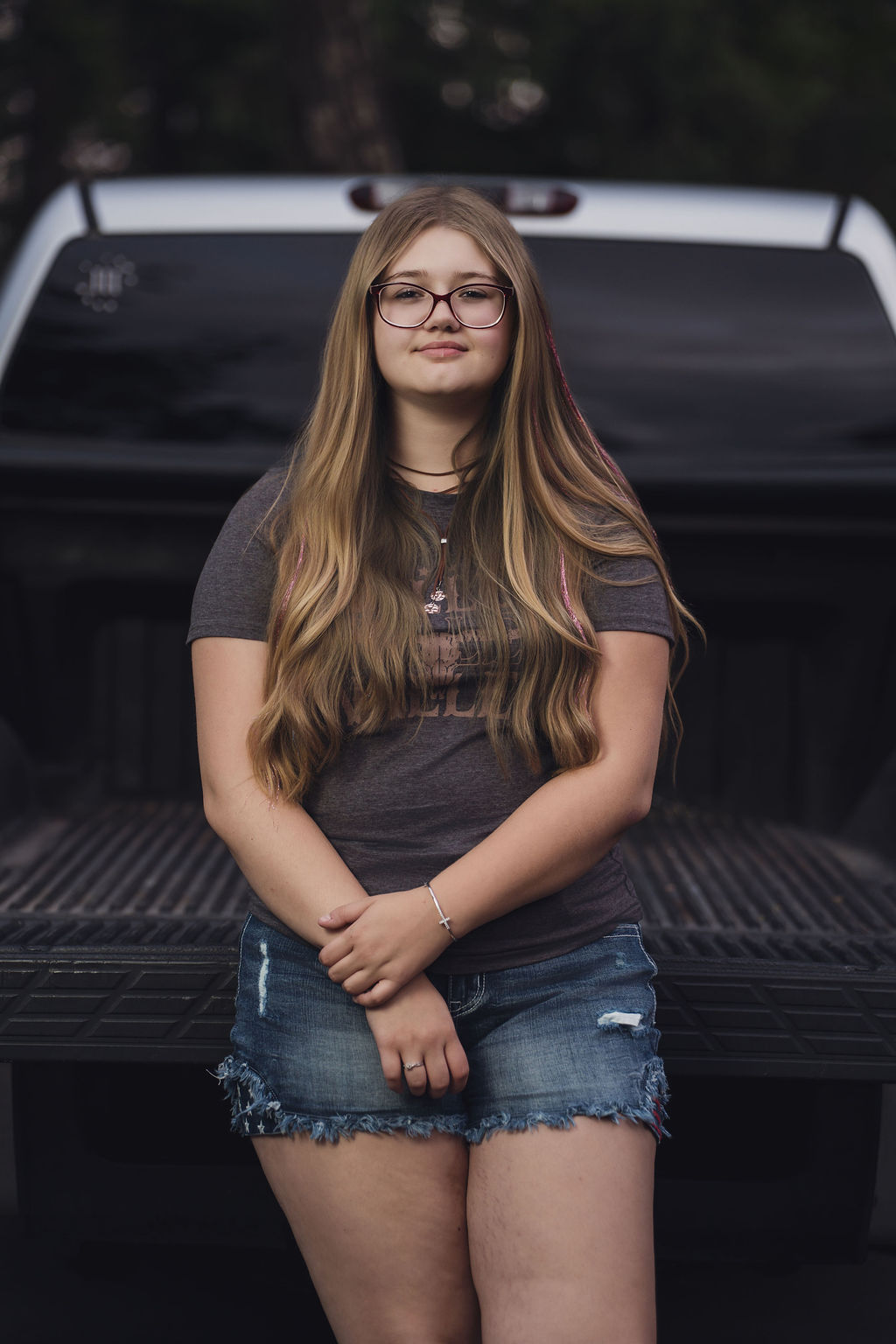 Senior in a graphic tee and denim shorts seated in the bed of her silver pickup at Belfair State Park