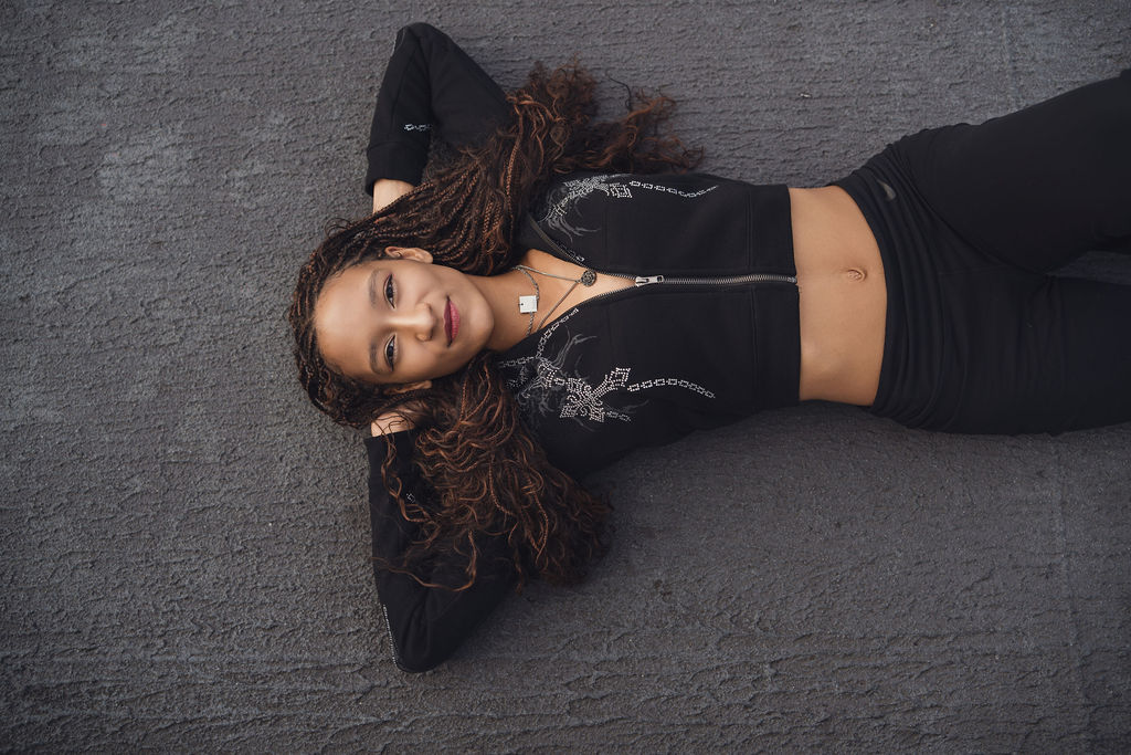 Overhead view of a high school senior lying on the deck with her arms behind her head and long curls spread across the pavement, a creative angle from a Seattle senior photographer.