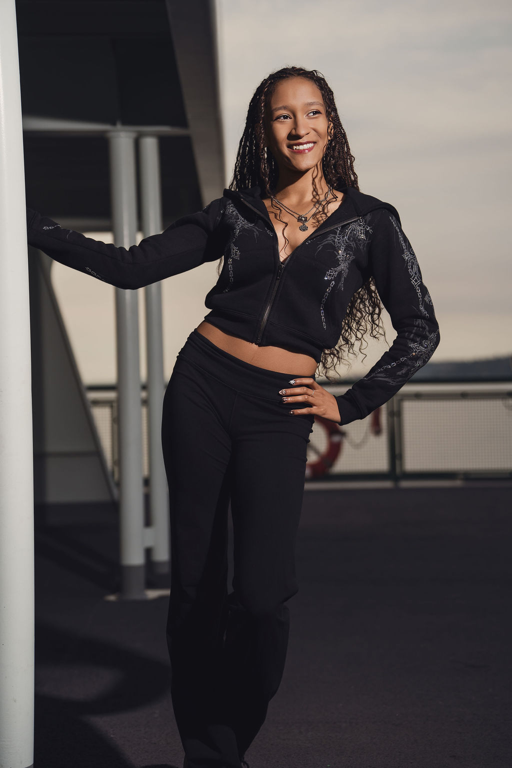 Smiling high school senior leaning against a white post on the upper deck of the Bremerton to Seattle ferry during her senior portrait session