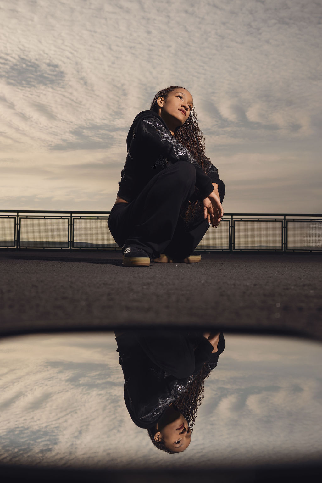 High school senior crouching on the ferry deck gazing toward the horizon beneath textured evening clouds during a Puget Sound senior session