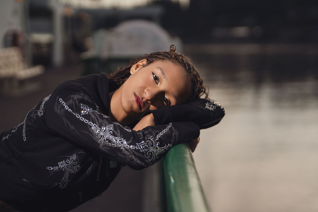 Close portrait of a high school senior resting her head on her arms along the green deck rail with soft golden light on the water, from a Bremerton senior photographer.
