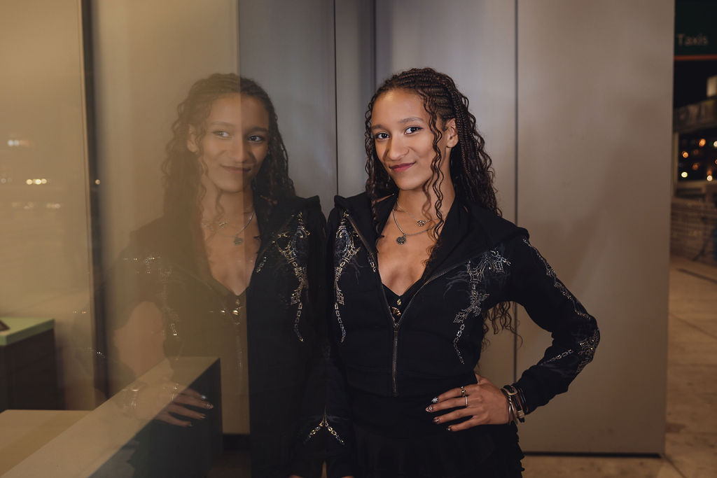 Smiling high school senior standing beside a glass wall that mirrors her reflection at a Seattle waterfront pier building, captured during an evening city senior session.