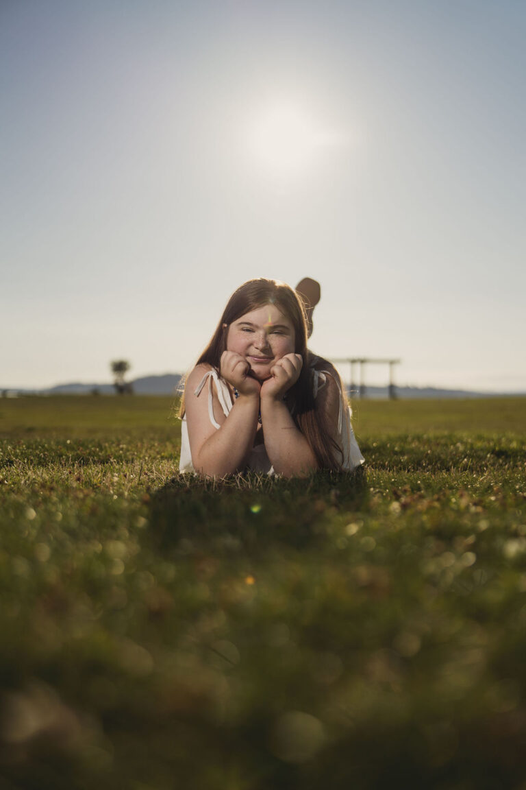 Tacoma senior photographer portrait of a high school senior lying in the grass with her chin on her hands at golden hour