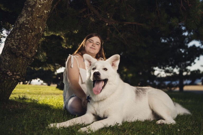 Senior kneeling beside her white husky at Chambers Bay during a Tacoma senior photographer session