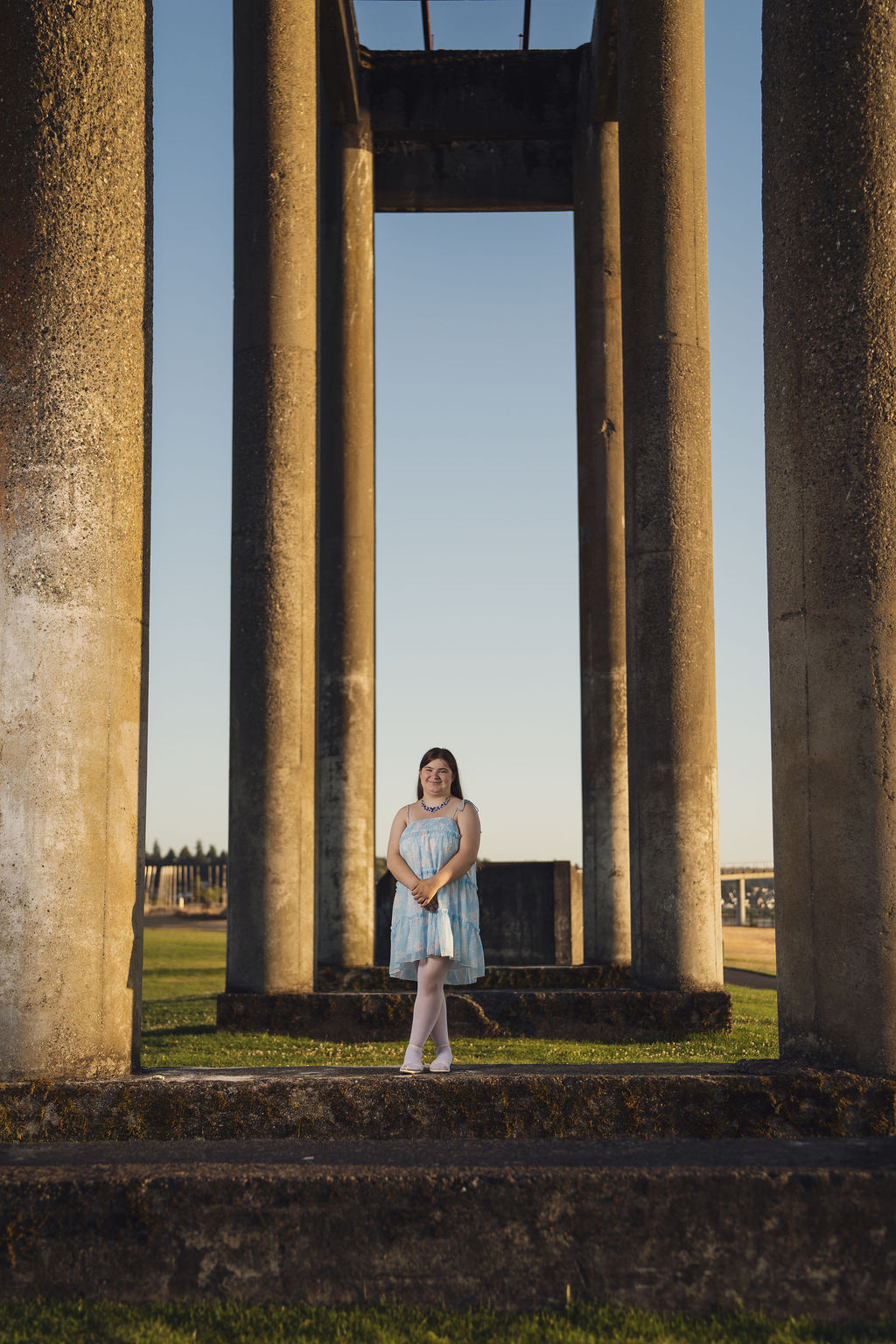 University Place senior photographer portrait of a senior standing among the tall concrete columns at Chambers Bay at golden hour
