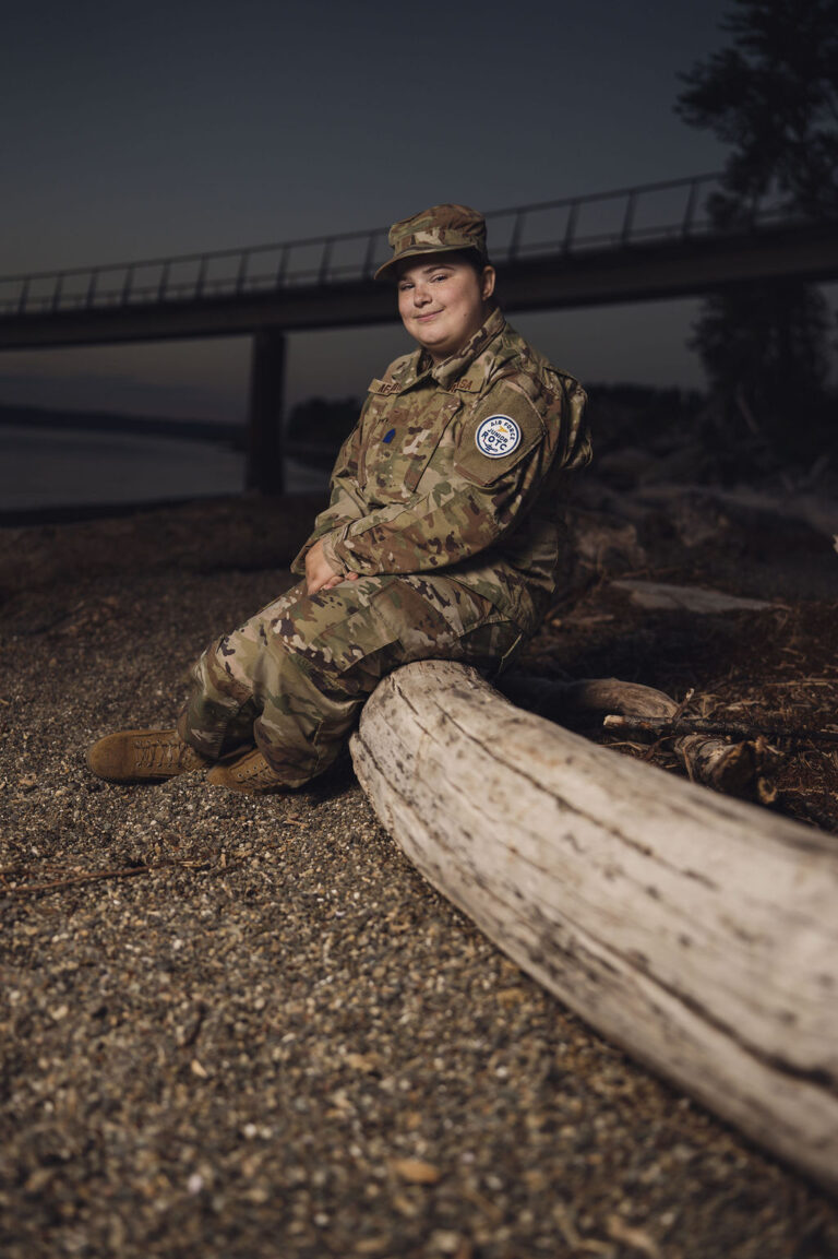 Tacoma senior photographer portrait of a senior in Air Force Junior ROTC uniform seated on driftwood with the Chambers Bay bridge behind