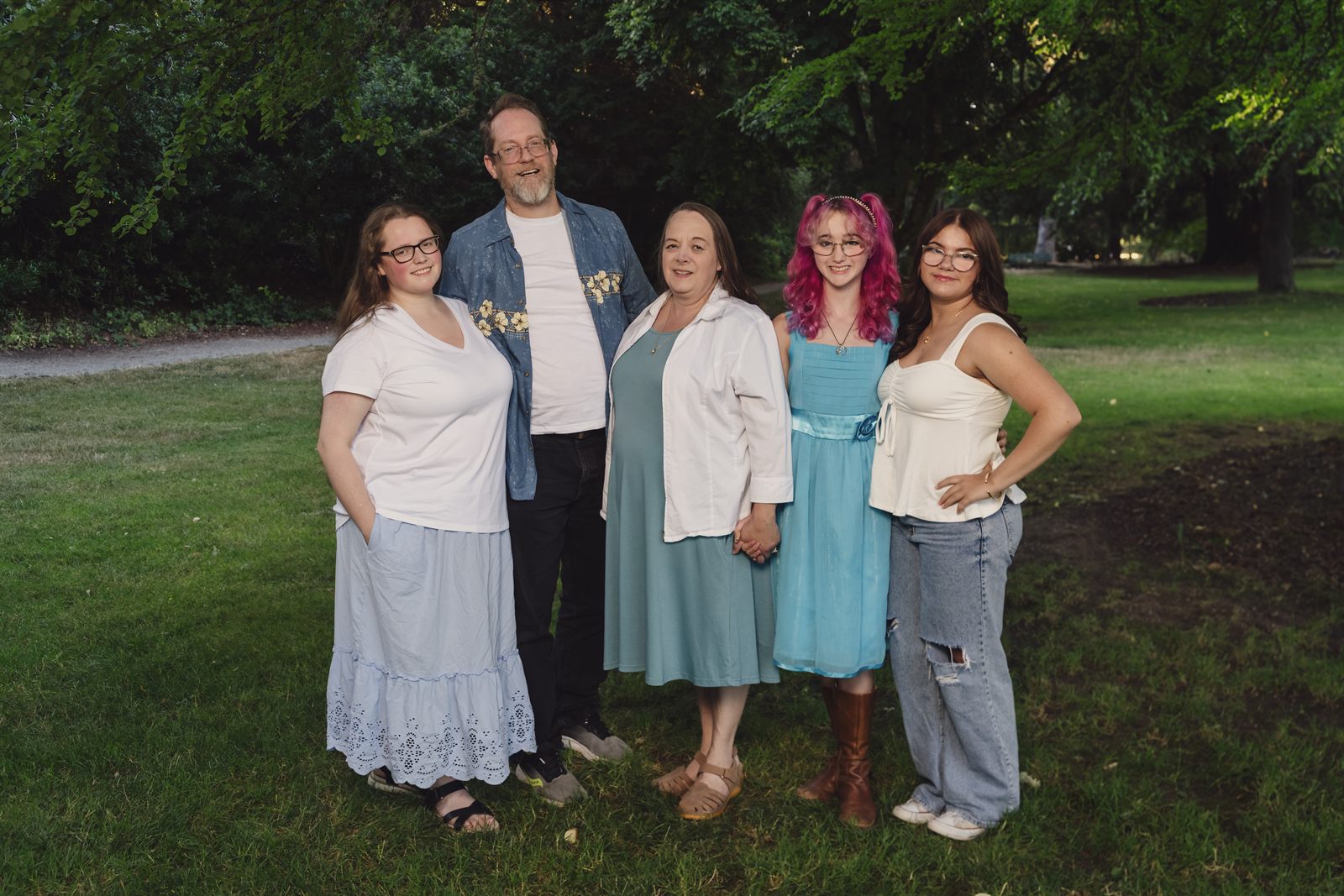 Family of five standing together on the lawn under mature shade trees at Point Defiance Park in Tacoma