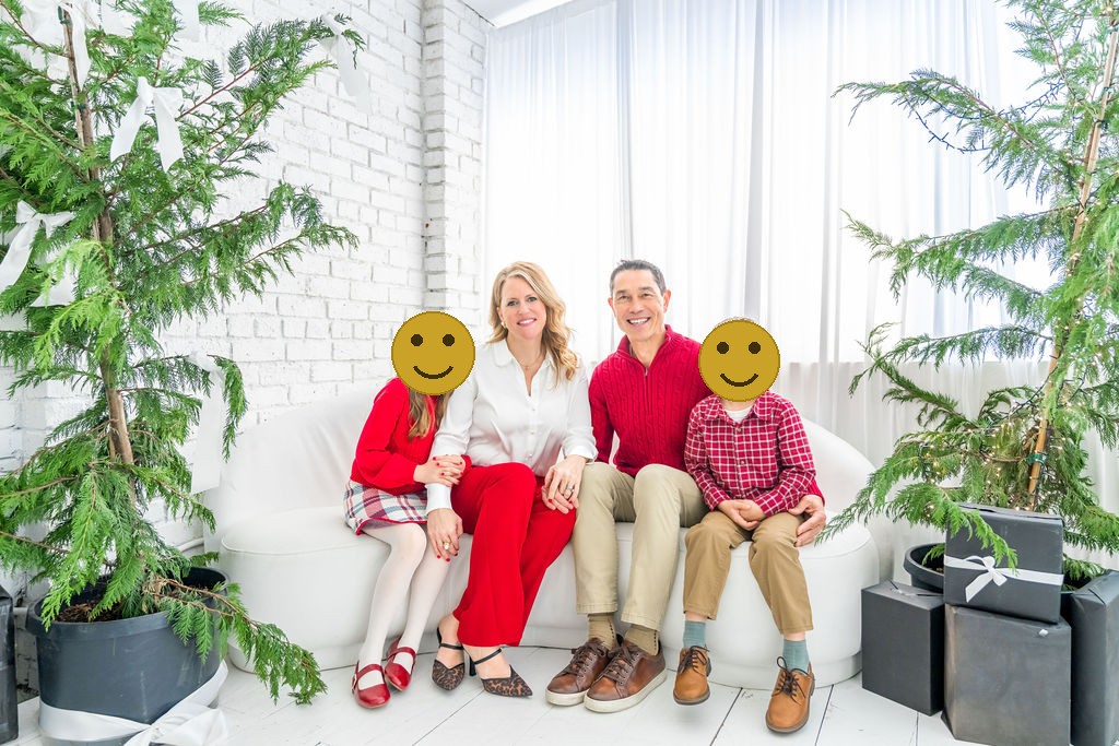 Family of four on a white couch surrounded by fresh cedar trees during a holiday studio session in Bremerton, faces covered for privacy