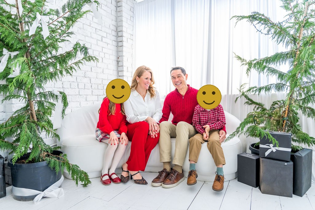 Family of four relaxed together on a white couch surrounded by cedar trees during a holiday studio session in Bremerton