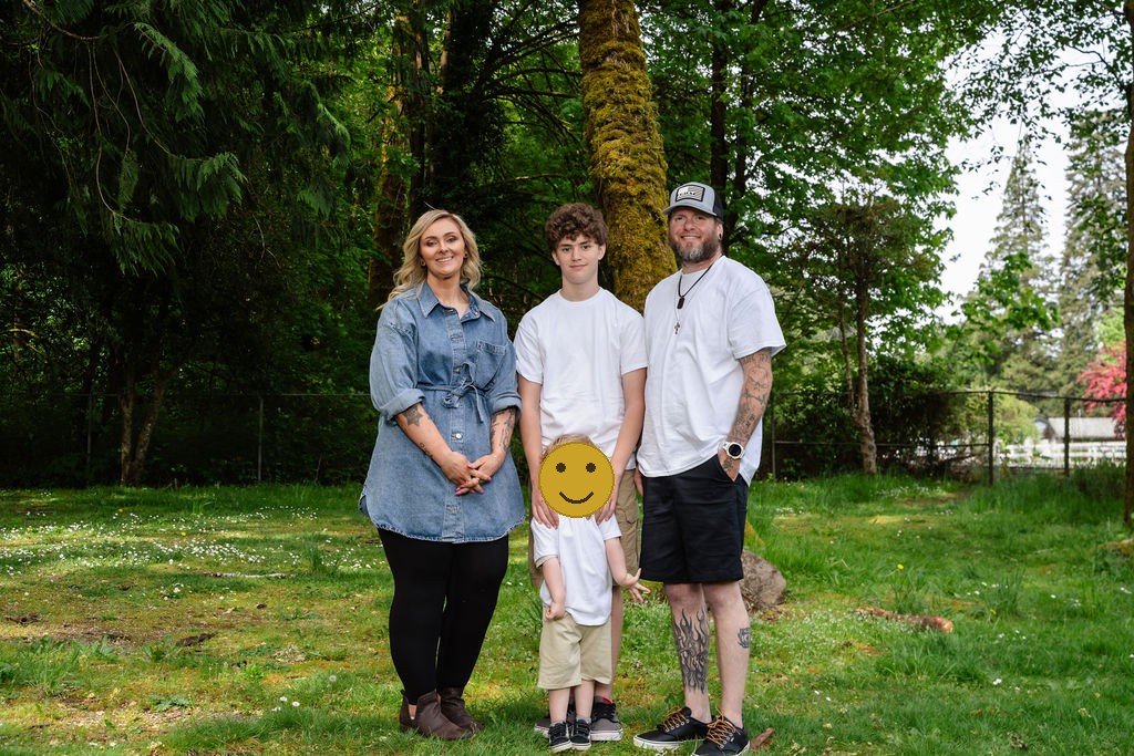 Family of four with two young sons posing among the trees at a green Kitsap County park