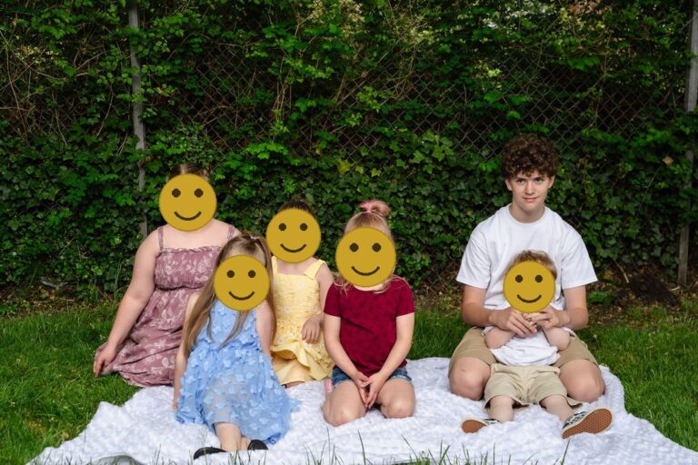 Six cousins sitting together on a white blanket in front of leafy greenery at a Kitsap County park