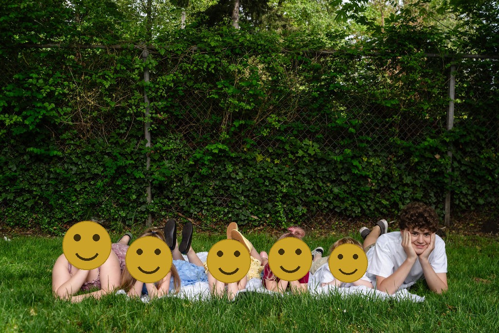 Six children lying in a row in the grass with their chins on their hands at a Kitsap County park, faces covered for privacy