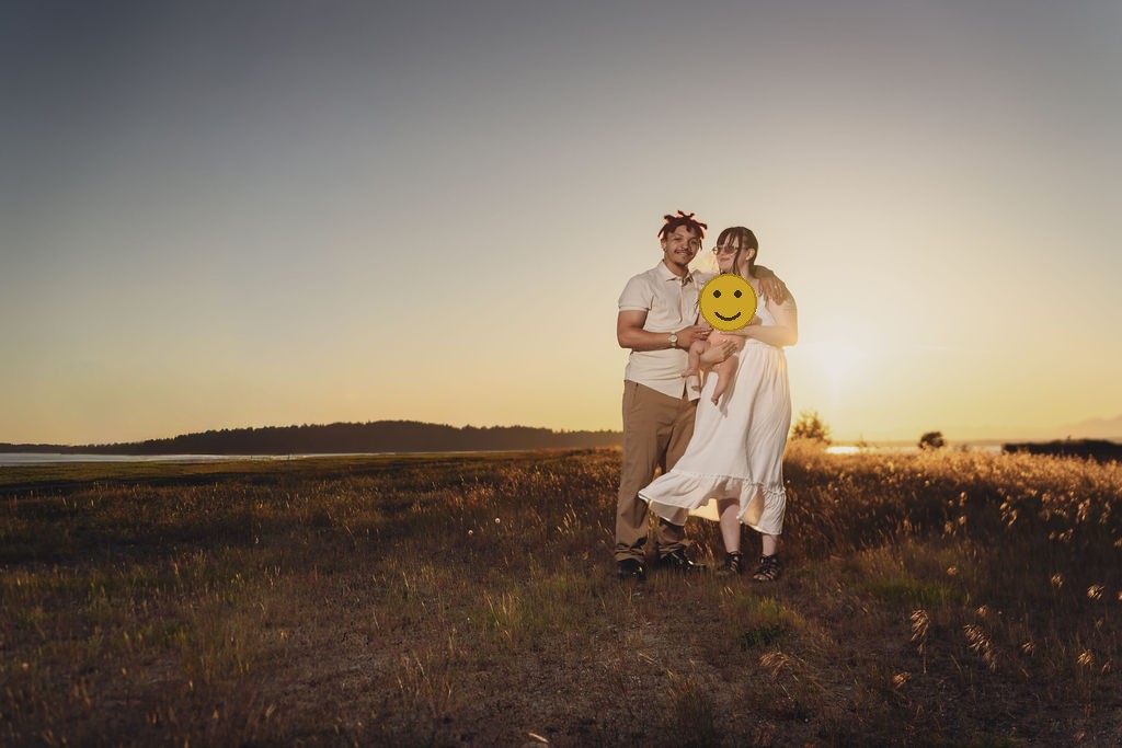 Engaged couple holding their infant daughter in a golden meadow at sunset at Chambers Bay near Tacoma