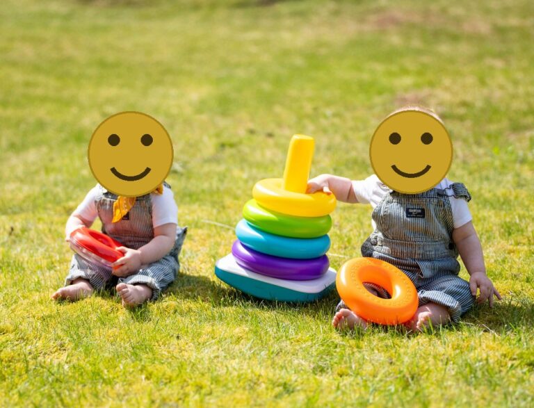Twin babies in striped overalls playing with a stacking ring toy in the grass during an outdoor family session in Kitsap County