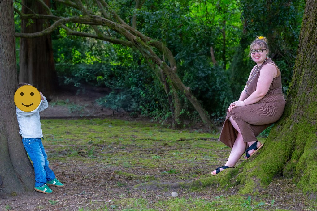 Young boy peeking around a tree while his mother rests nearby at a Kitsap County park