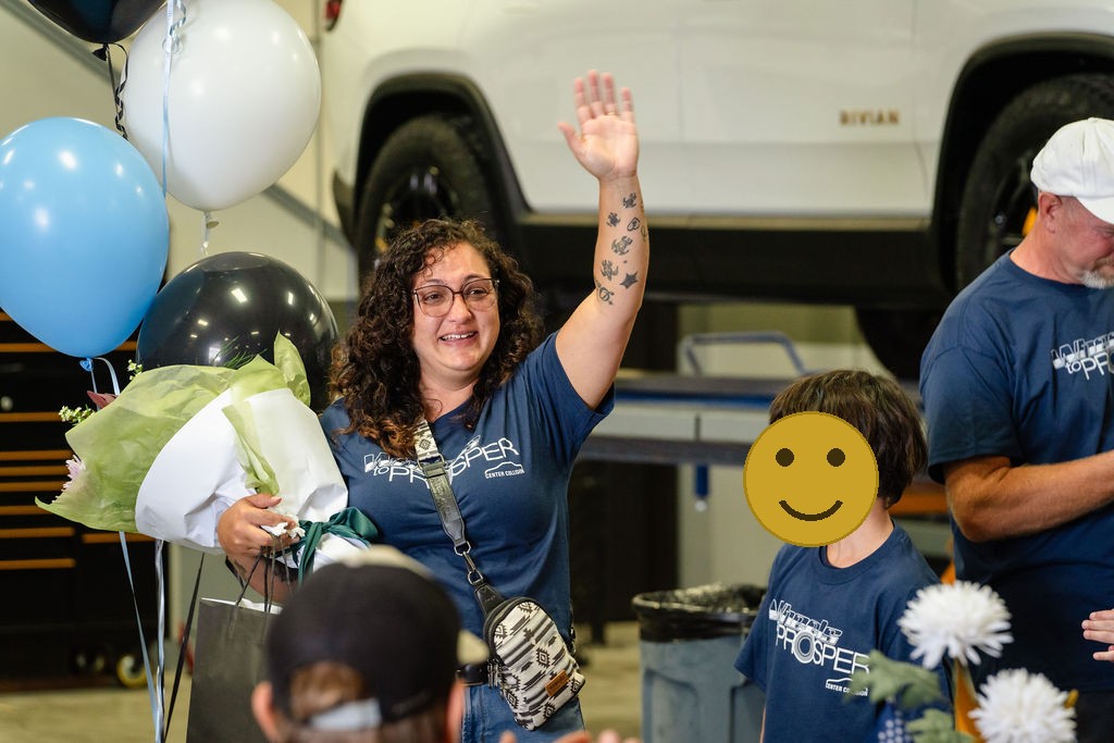 Mother waving and holding flowers at a Tacoma charity car giveaway celebration