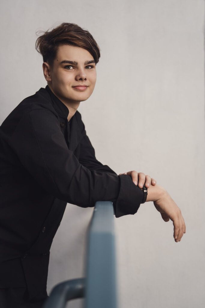 High school senior in a chef coat leaning on a blue railing for a clean portrait during a Bremerton senior session