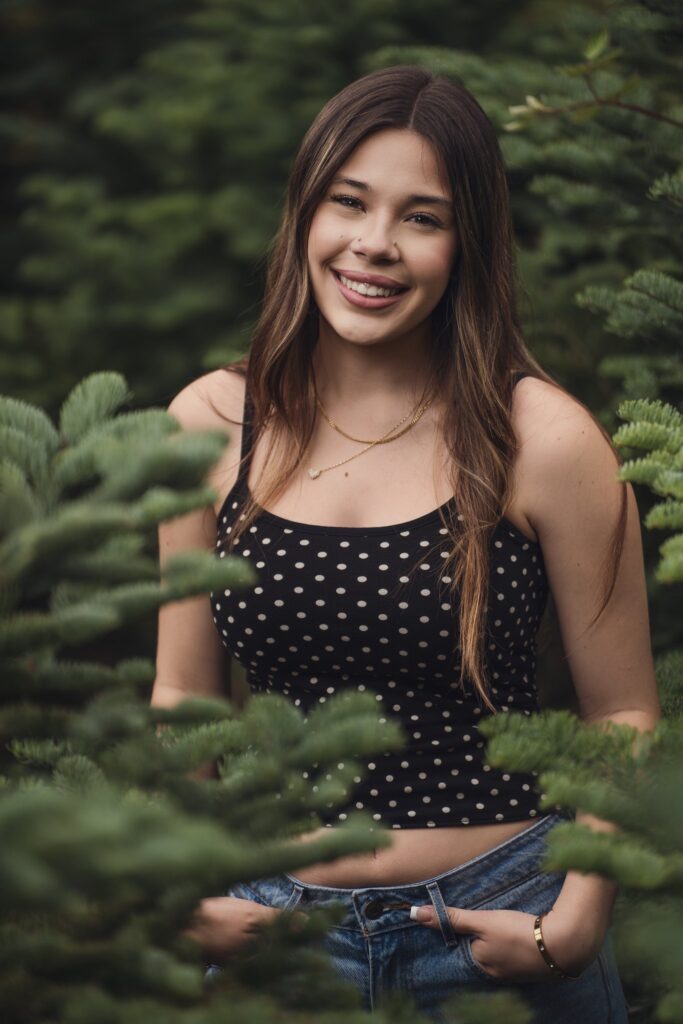 High school senior in a polka dot top framed by evergreen boughs on the trail near Bremerton