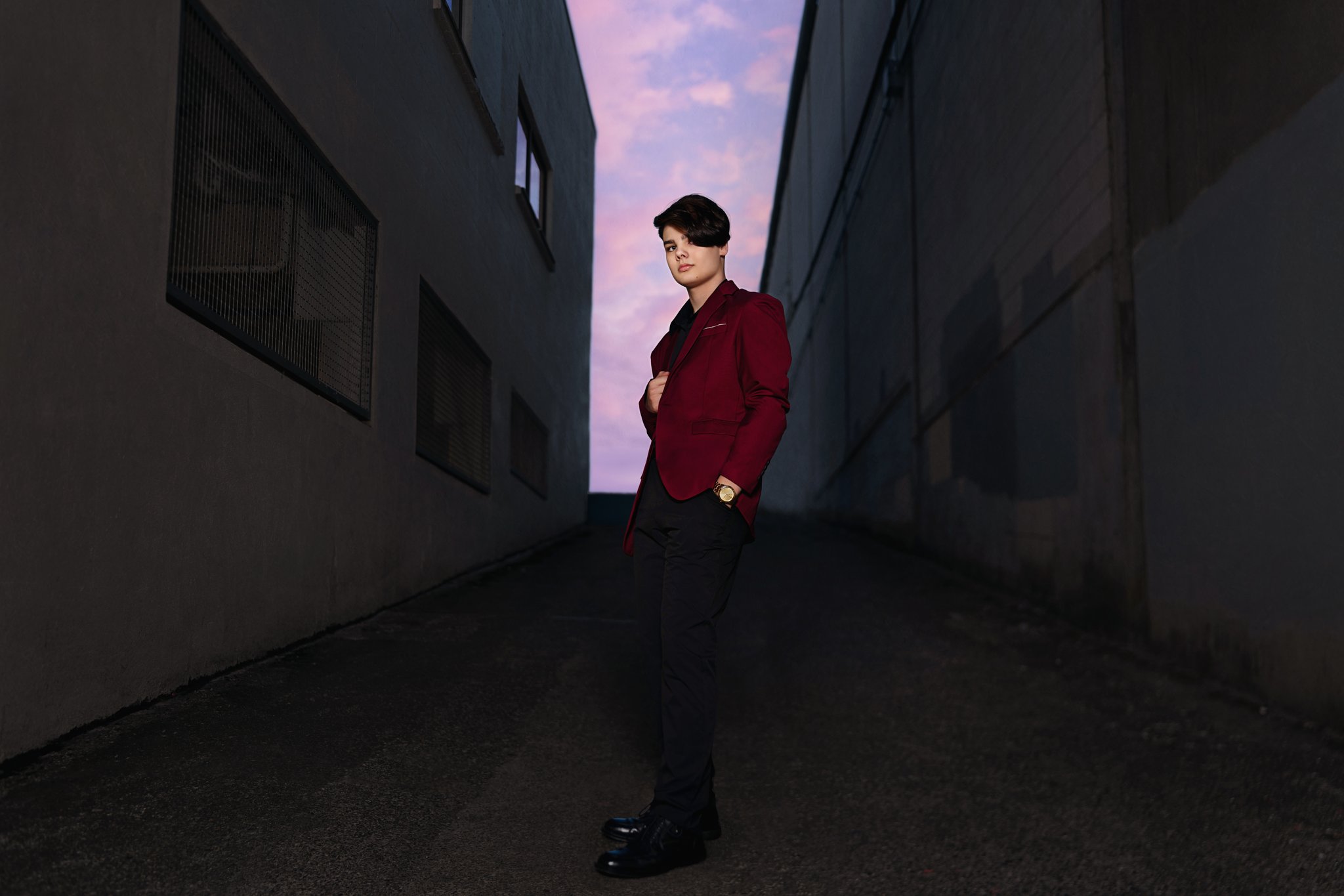 High school senior in a burgundy blazer standing in a downtown Bremerton alley beneath a pink dusk sky Photographed by Bremerton senior photographer Nautical Moments Photography.