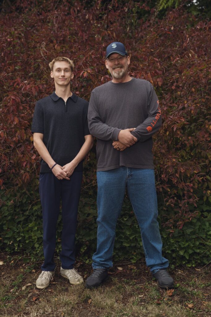 High school senior and his dad standing together in front of red autumn leaves at Smith Childrens Park in Bremerton