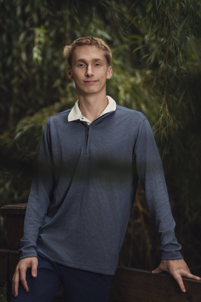 High school senior portrait framed by willow branches on a footbridge at Smith Childrens Park in Bremerton