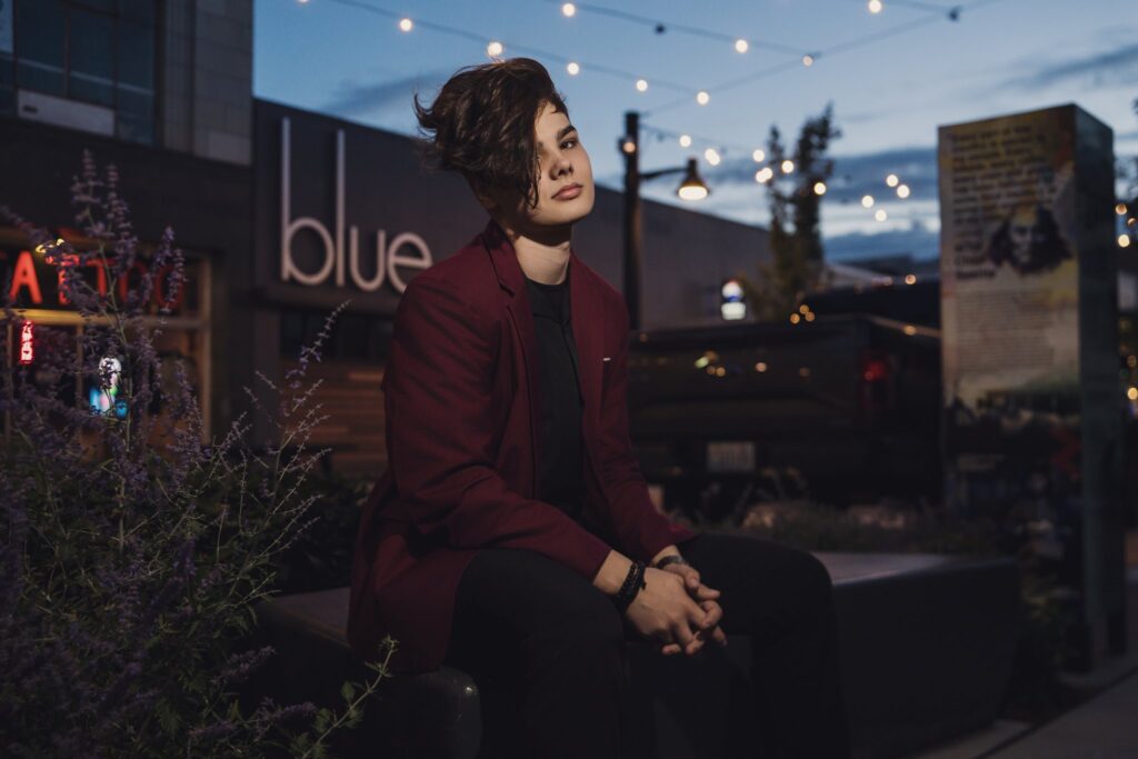 High school senior in a burgundy blazer seated among purple blooms under string lights at Quincy Square in downtown Bremerton at dusk