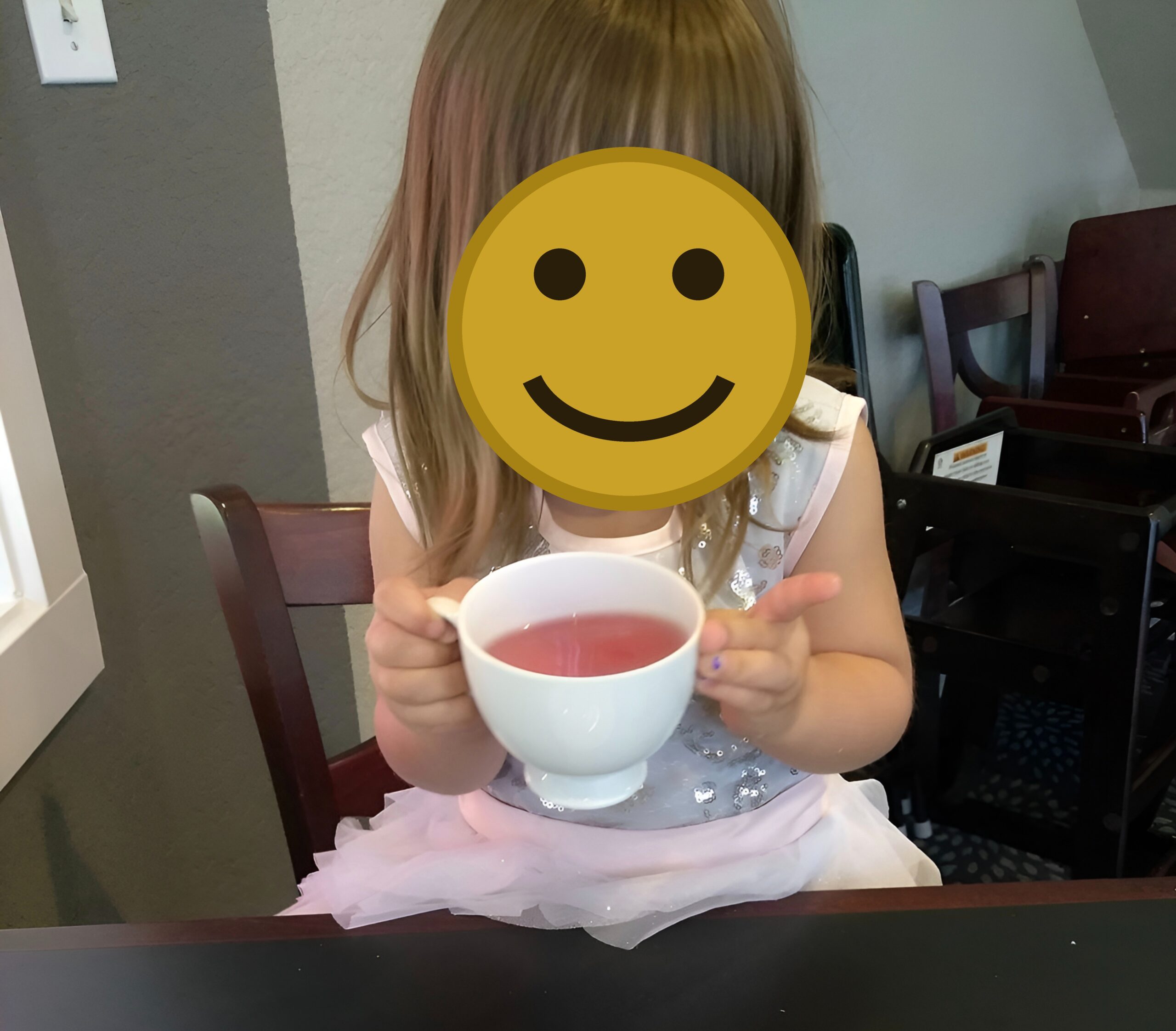 Ava my little girl with a tea cup smiling, faces covered for privacy