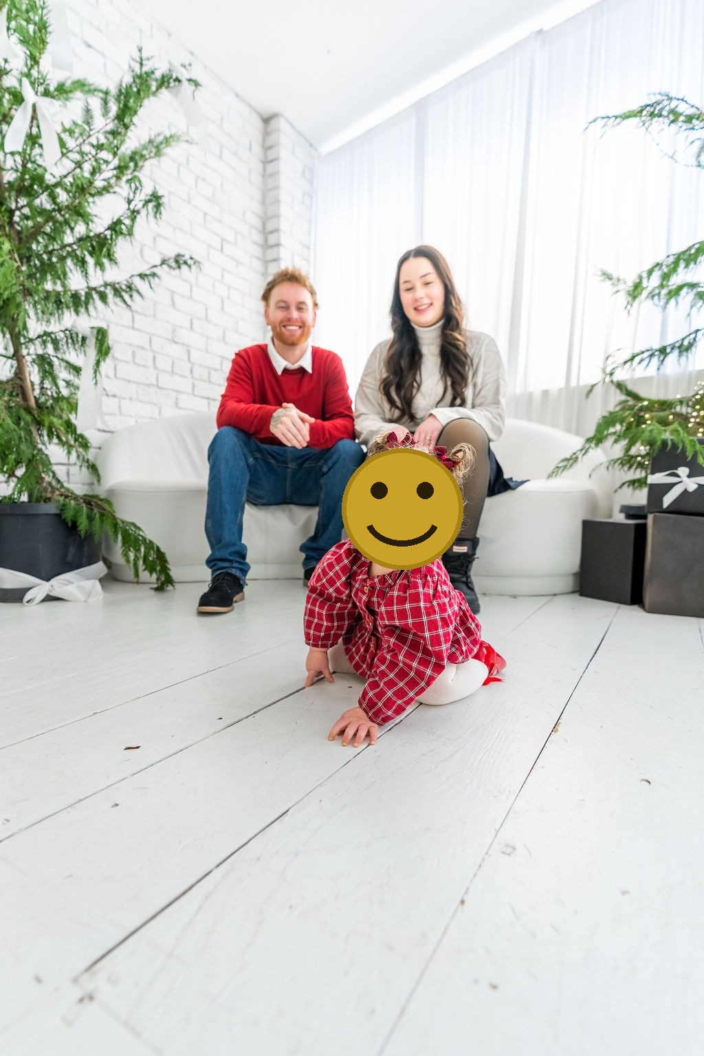 Toddler crawling toward the camera while her parents sit behind her during an indoor family studio session in Washington