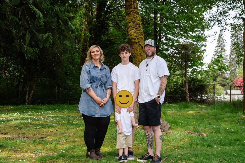 Family of four standing together under tall trees at Evergreen Rotary Park in Bremerton, faces covered for privacy