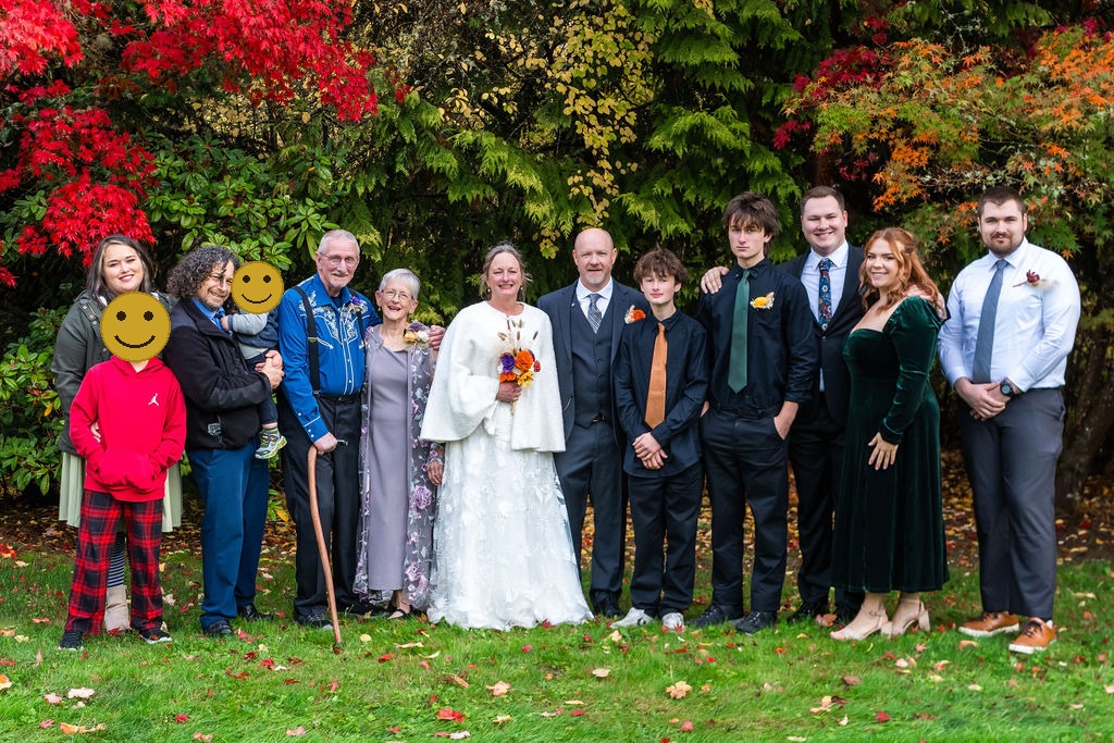 Bride and groom standing with extended family members for a large family portrait in front of colorful autumn trees during a Vashon Island wedding, faces covered for privacy